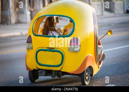 Scene di strada attraverso la città vecchia di l'Avana, Cuba. Un taxi a motore unico porta le persone intorno all'Avana; l'Avana, l'Avana, Cuba Foto Stock