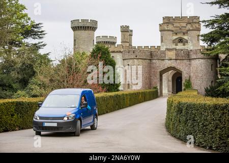 Donna seduta in un camper che guarda fuori dalla finestra e visita turistica di fronte al castello di Eastnor a Ledbury; Eastnor, Herefordshire, Inghilterra, Regno Unito Foto Stock