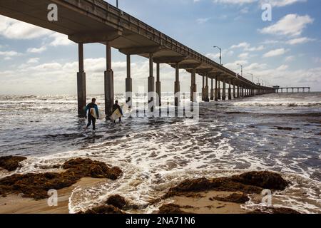 Surfisti che camminano in surf da una spiaggia sotto una strada sopraelevata a San Diego; San Diego, California, Stati Uniti d'America Foto Stock