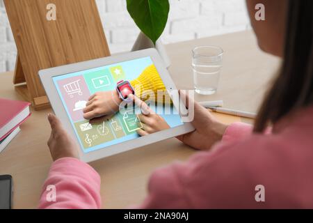 Controlla la geolocalizzazione dei bambini tramite l'orologio intelligente. Donna che usa la compressa a tavola, primo piano Foto Stock