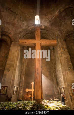 La luce del sole scorre nel monastero di Jvari su una croce, mentre una donna prega di fronte alla foto di un santo; Mtskheta, Georgiaq Foto Stock