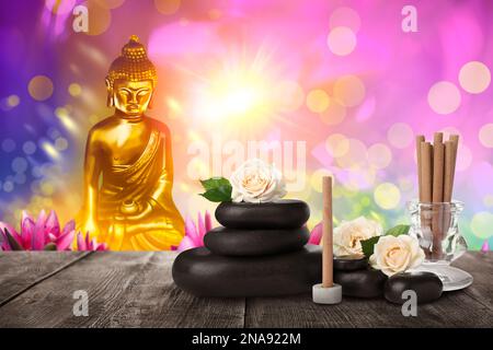 Composizione con bastoni d'incenso su tavolo di legno e figura di Buddha sullo sfondo Foto Stock