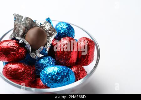 Ciotola di vetro con uova di cioccolato avvolte in foglio colorato su sfondo bianco, primo piano Foto Stock