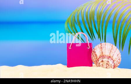 Borsa rosa per lo shopping o il regalo con conch su sabbia bianca, dietro il mare con palme. Concetto di riposo, viaggio, shopping, vacanza in caldo paese. Centro di copiatura Foto Stock