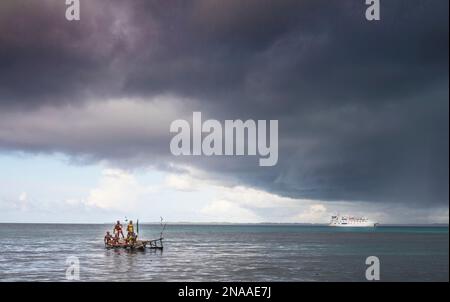 Outrigger canoa sotto il cielo tempestoso al largo della costa dell'isola di Kuiawa con nave da crociera spedizione nelle isole Trobriand, Papua Nuova Guinea Foto Stock