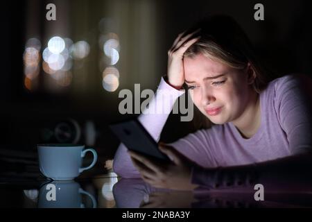 Triste teen che piange il telefono di controllo nella notte a casa Foto Stock