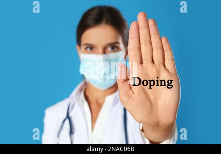 Medico nella maschera protettiva che mostra il gesto di arresto su sfondo blu, fuoco a portata di mano. Controllo del doping Foto Stock