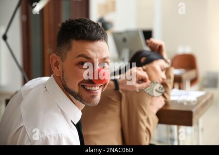 Uomo con il naso di clown che attacca il pesce di carta alla schiena della collega mentre dorme in ufficio. Scherzo divertente Foto Stock