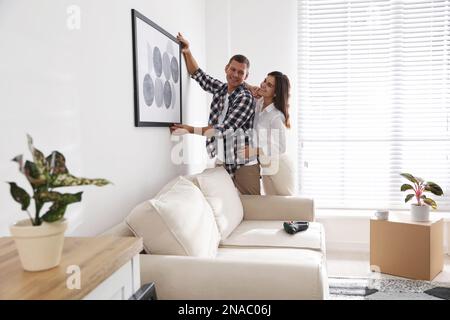 Felice coppia appendere l'immagine sul muro bianco insieme. Design degli interni Foto Stock