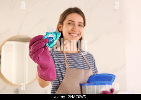 Donna felice che tiene la capsula di detersivo del bucato all'interno, fuoco sulla mano Foto Stock