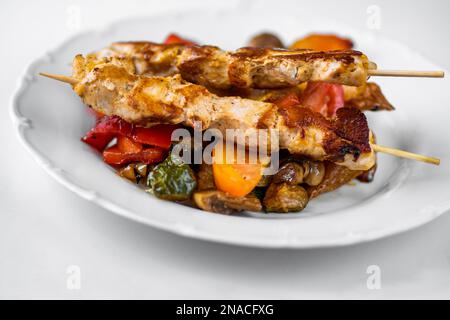 Carne di maiale su spiedino (souvlaki) su verdure succulente al forno. Delizioso pranzo o cena greca, primo piano. Foto Stock