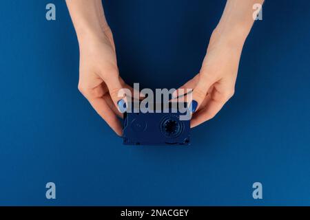 Mini videocassetta in mani femminili su sfondo blu classico Foto Stock