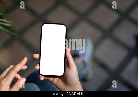 Immagine ravvicinata della mano di una donna che tiene in mano uno smartphone bianco schermo mockup per visualizzare il banner grafico sullo schermo su sfondo sfocato. Foto Stock