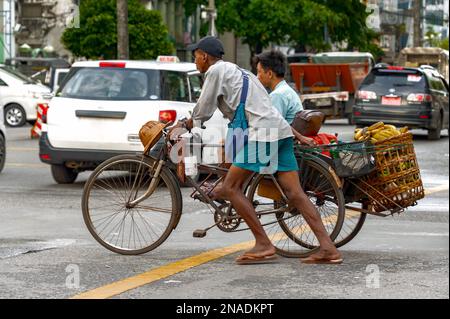 China Town, Yangon - 21 ottobre 2017: Un tassista triciclo spinge con attenzione il suo triciclo caricato con un cesto pieno di banane e un passeggero. Foto Stock