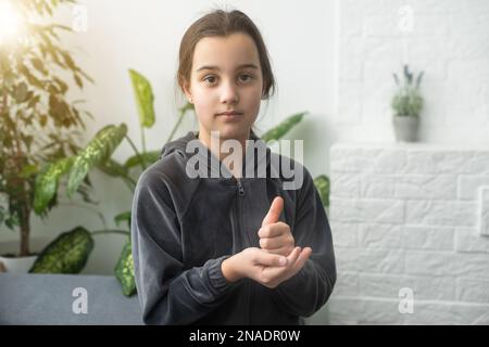 Carino sordomuto ragazza utilizzando il linguaggio dei segni su sfondo chiaro Foto Stock