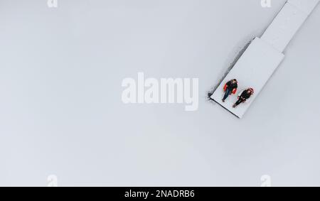 Coppia seduta in sedie alla fine del molo nevoso il giorno d'inverno. Foto Stock