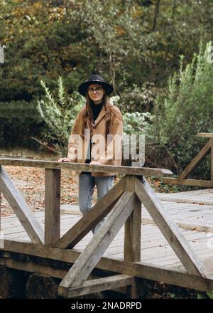 giovane donna in giacca marrone e cappello nero nella foresta Foto Stock