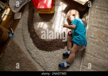 Bambino addormentato sul pavimento vicino al materasso Foto Stock