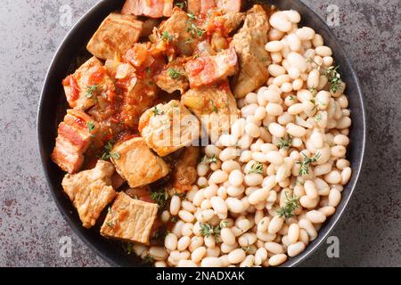 Arrosto di maiale con pancetta, pomodoro e cipolla con fagioli bianchi guarnire in un piatto sul tavolo. Vista orizzontale dall'alto Foto Stock