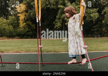 La giovane ragazza gioca sul parco giochi attrezzature nel giorno nuvoloso Foto Stock