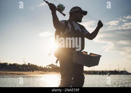 Uomo ispanico pesca a mosca in oceano al largo della spiaggia nel pomeriggio Foto Stock