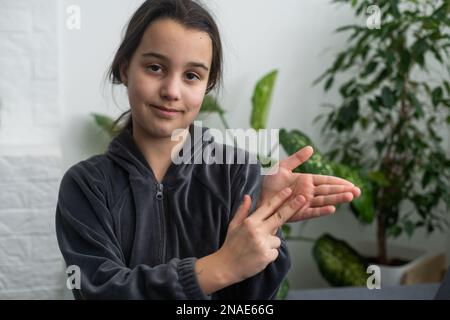 Carino sordomuto ragazza utilizzando il linguaggio dei segni su sfondo chiaro Foto Stock