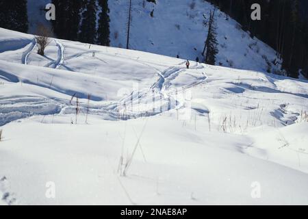 Un escursionista cammina lungo sentieri innevati in una valle di montagna. Foto Stock