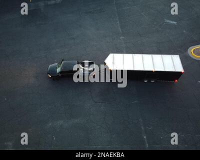 Una ripresa aerea di un pickup car con un rimorchio che trasferisce i prodotti sull'asfalto nero Foto Stock