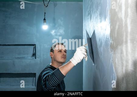 l'uomo applica l'isolamento a una parete del bagno con cazzuola Foto Stock