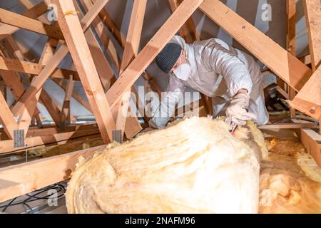 l'uomo isola il tetto e il soffitto della casa con lana di vetro Foto Stock