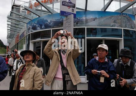 I turisti giapponesi si riuniscono e scattano foto dalla piazza principale di Zermatt, dove possono vedere il famoso picco piramidale quasi simmetrico, la questione... Foto Stock