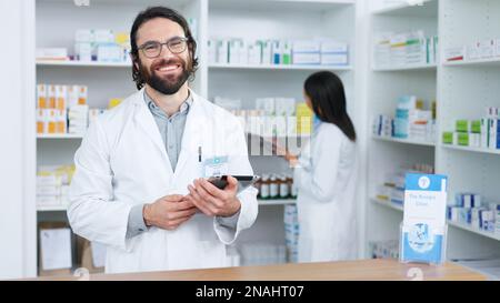 Ritratto di un farmacista allegro e amichevole utilizzando un tablet digitale per controllare l'inventario o gli ordini online in un chimico. Giovane uomo caucasico che usa Foto Stock