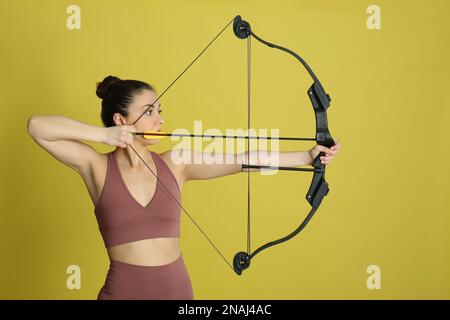 Donna con arco e freccia pratica tiro con l'arco su sfondo giallo Foto Stock