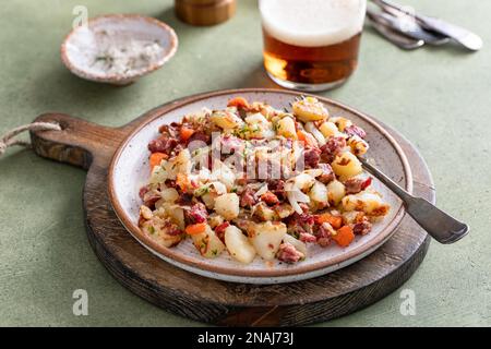 Hash di manzo con patate, cavolo e carota su un piatto servito con birra Foto Stock