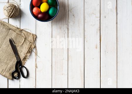 Arcobaleno colore uova di pasqua in una ciotola. Forbici, tessuto di iuta, corda su sfondo di legno. Direttamente sopra il piano del tavolo. Foto Stock