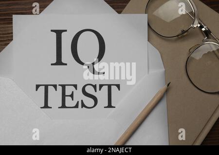 Carta con parole IQ Test in busta, matita, notebook e bicchieri su tavolo di legno, piatto Foto Stock