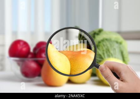 Donna con lente d'ingrandimento esplorando frutta, primo piano. Rilevamento di veleni Foto Stock