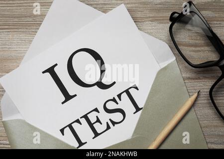 Carta con parole IQ Test in busta, matita e bicchieri su tavolo di legno, piatto Foto Stock