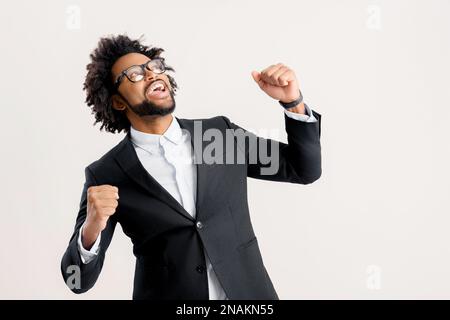 Overjoyed eccitato afro-americano imprenditore maschio, manager o proprietario di affari in abito nero casual intelligente gridare sì in segno di successo, in piedi su isolato su bianco, felice di vincere o ottenere profitto Foto Stock
