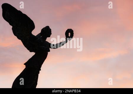 Statua della vittoria alata contro le nuvole rosa all'altare della Patria a Roma, Italia. Vista serale della statua in bronzo che tiene una corona a foglia di alloro Foto Stock