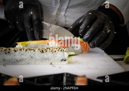 Foto di sushi preparati e confezionati per essere consegnati, con un focus sulle mani di uno chef sushi. Foto Stock