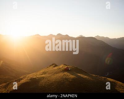 Panorama al tramonto di rosso idilliaco montagna alpina solitaria Brewster Hut arroccato sulla cima di collina erba in alto sopra la valle del fiume Haast, West Coast so Foto Stock