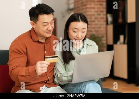Eccitato asiatico uomo e donna utilizzando computer portatile e carta di credito di plastica, pagando per beni e servizi online Foto Stock