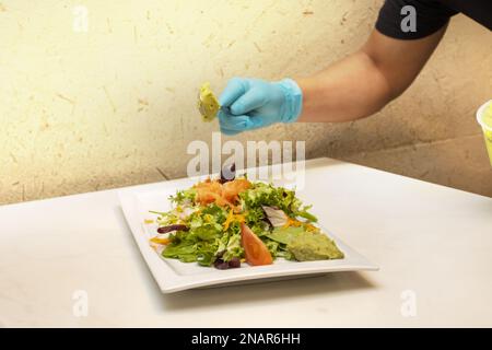 Uno chef prepara un piatto di insalata con pomodoro, olive e guacamole Foto Stock