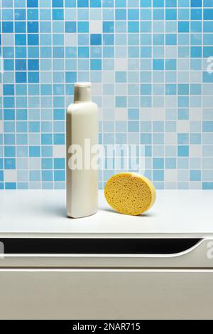 Una bottiglia di shampoo da 1 litro con una spugna sintetica gialla su un mobile bagno bianco e piastrelle blu Foto Stock