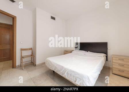 camera da letto con un grande letto con lenzuola bianche, testata in legno nero e comodini in legno Foto Stock