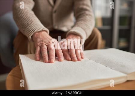 Primo piano di un uomo anziano seduto al tavolo a casa e leggendo un libro in Braille con le mani Foto Stock