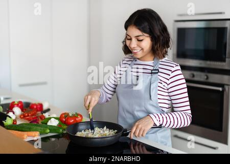 Bella giovane donna che mescola riso con verdure in padella Foto Stock