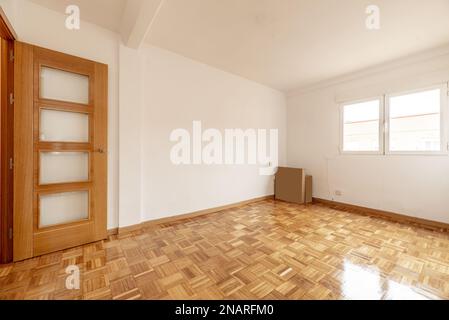 Soggiorno vuoto di un appartamento con pavimento in parquet in doghe di quercia appena stabbinate e verniciate, pareti lisce dipinte di bianco e porte in legno di Foto Stock