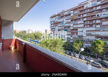 lunga e stretta terrazza con vernice rossa e vista su una strada fiancheggiata da alberi e altri edifici Foto Stock